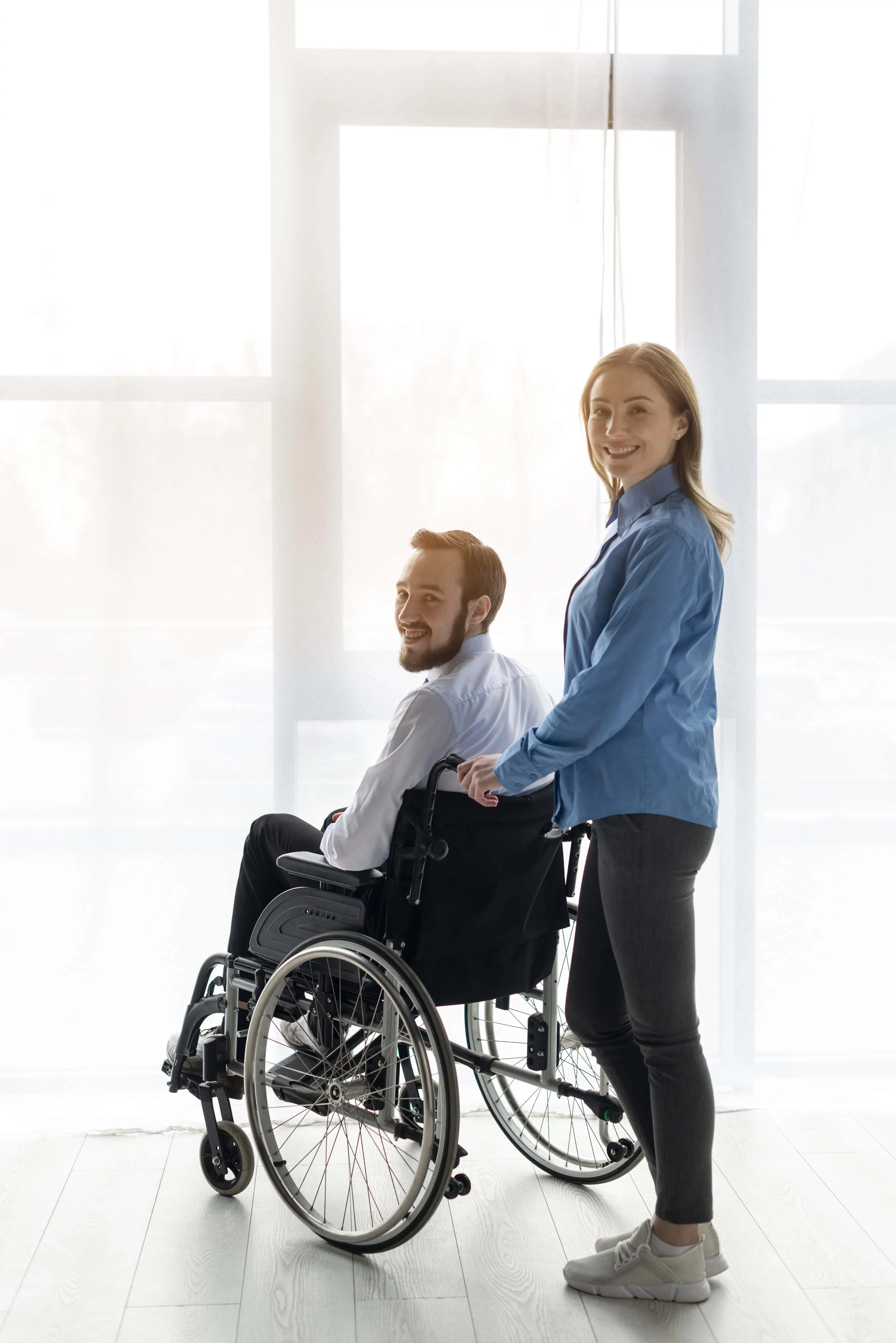 homem em cadeira de rodas sendo conduzido por cuidadora em ambiente interno iluminado